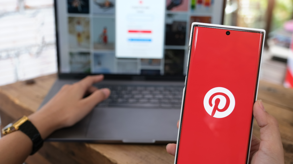 a mobile phone in the foreground with the pinterest logo showing and a laptop in the background