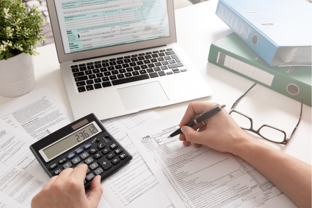 a person using a calculator and writing sat in front of a laptop