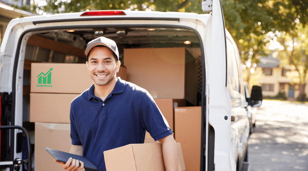 A smiling courier holding a parcel pictured behind a delivery van loaded with parcels