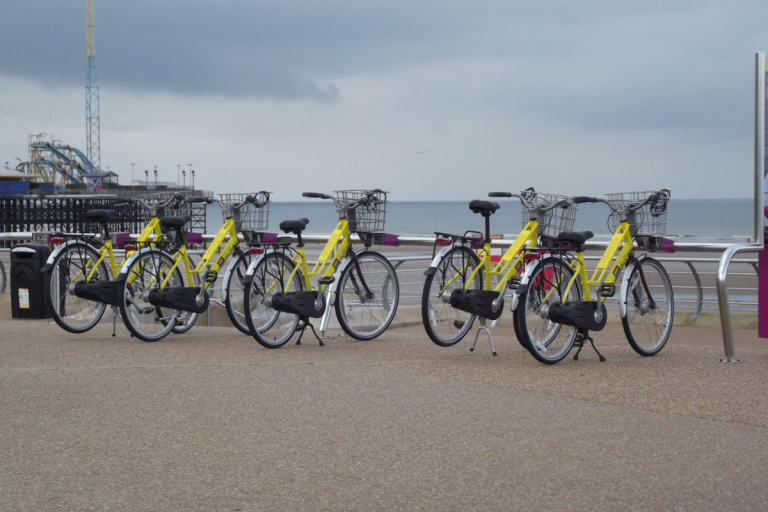 a row of five e-bikes for hire along a coastal promenade